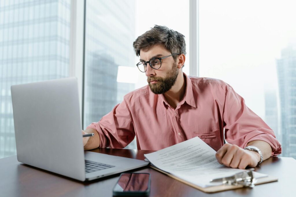 man in red dress shirt wearing black framed eyeglasses using macbook air